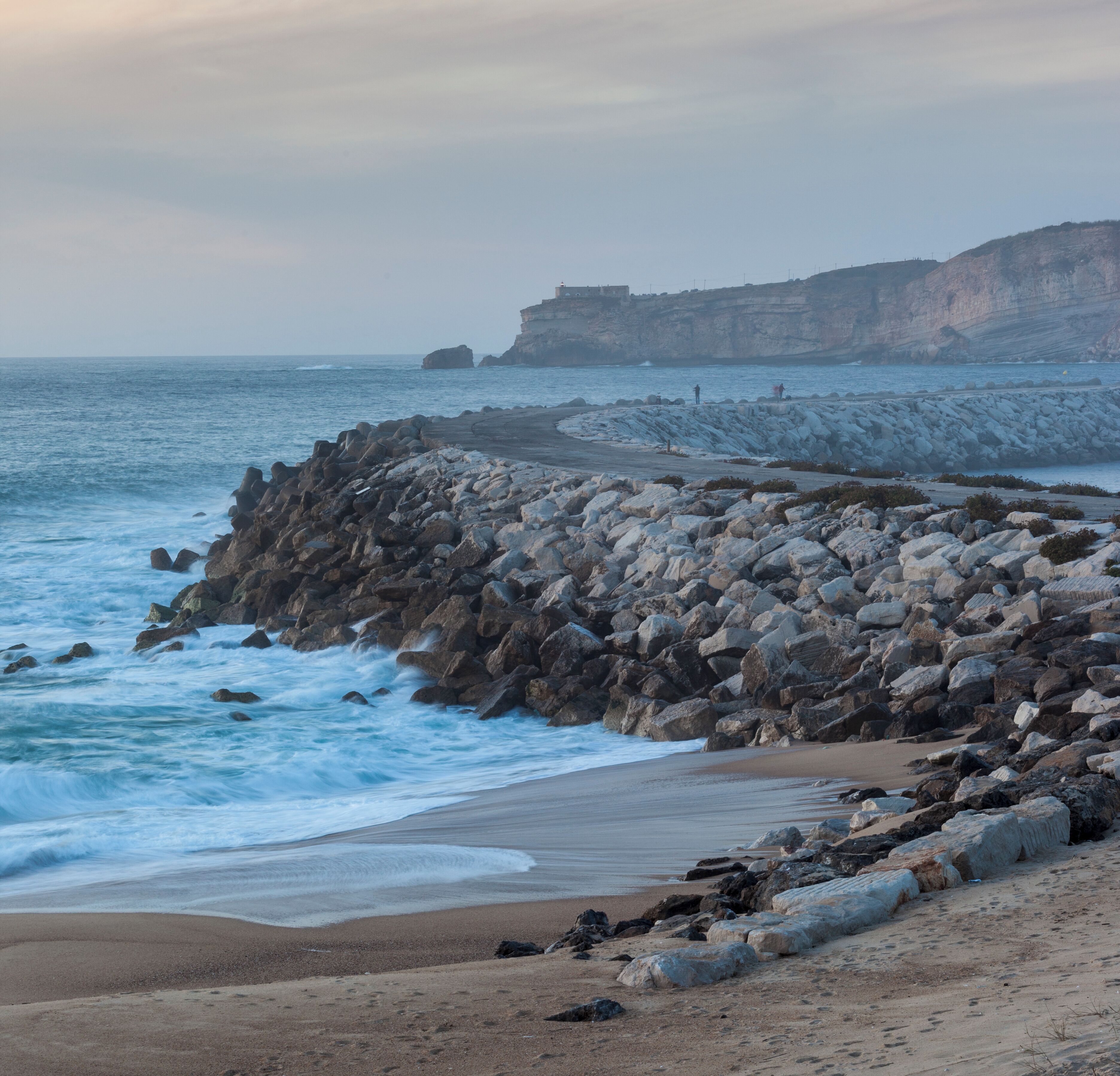 A rocky coastline with waves crashing against the shore and cliffs in the background.