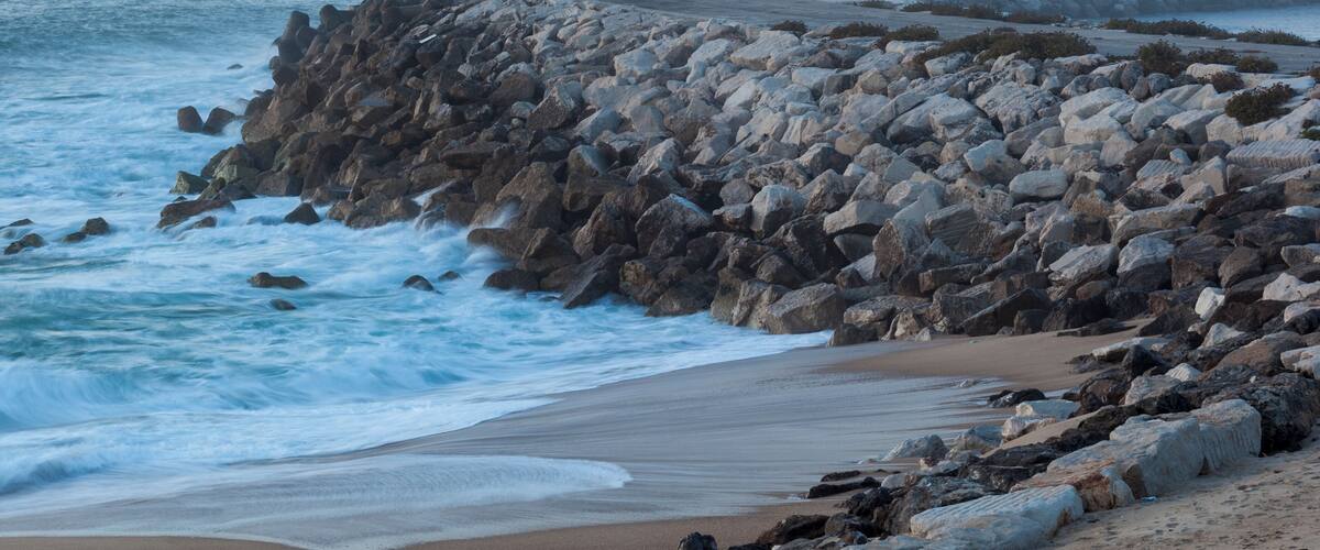 A rocky coastline with waves crashing against the shore and cliffs in the background.