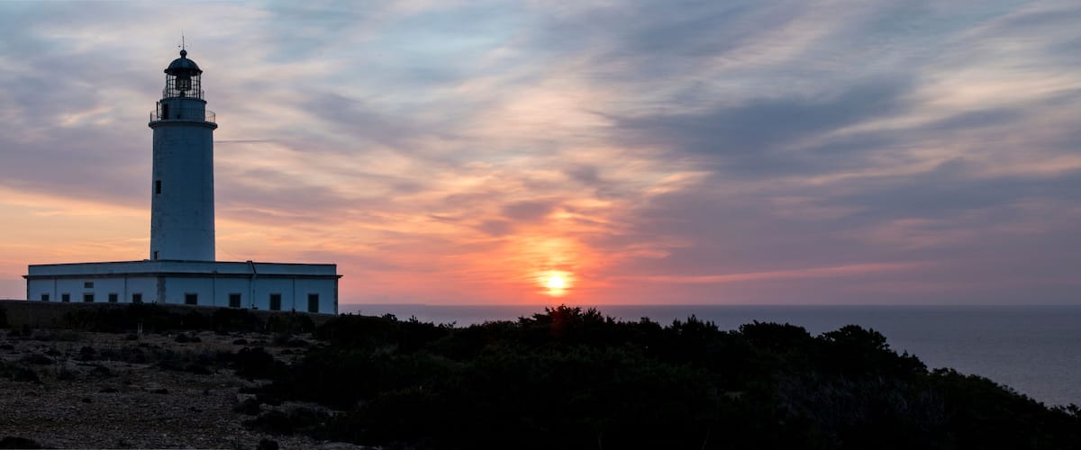 A lighthouse at sunset with a clear sky and ocean in the background.