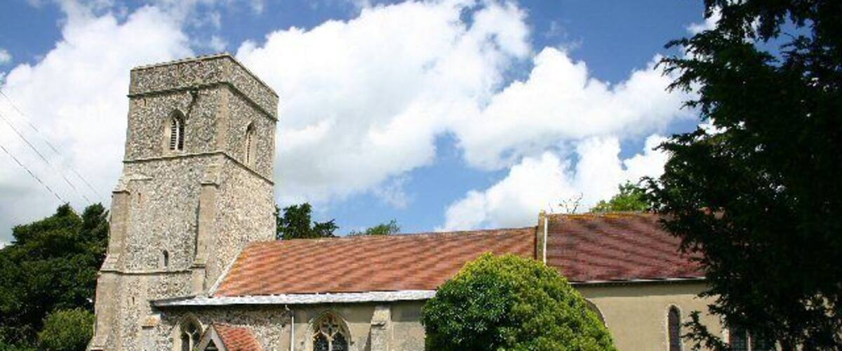 A church with a tower and a red-tiled roof, surrounded by greenery.