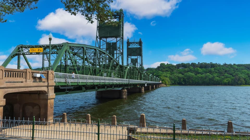 A green metal bridge over a river with a clear sky.