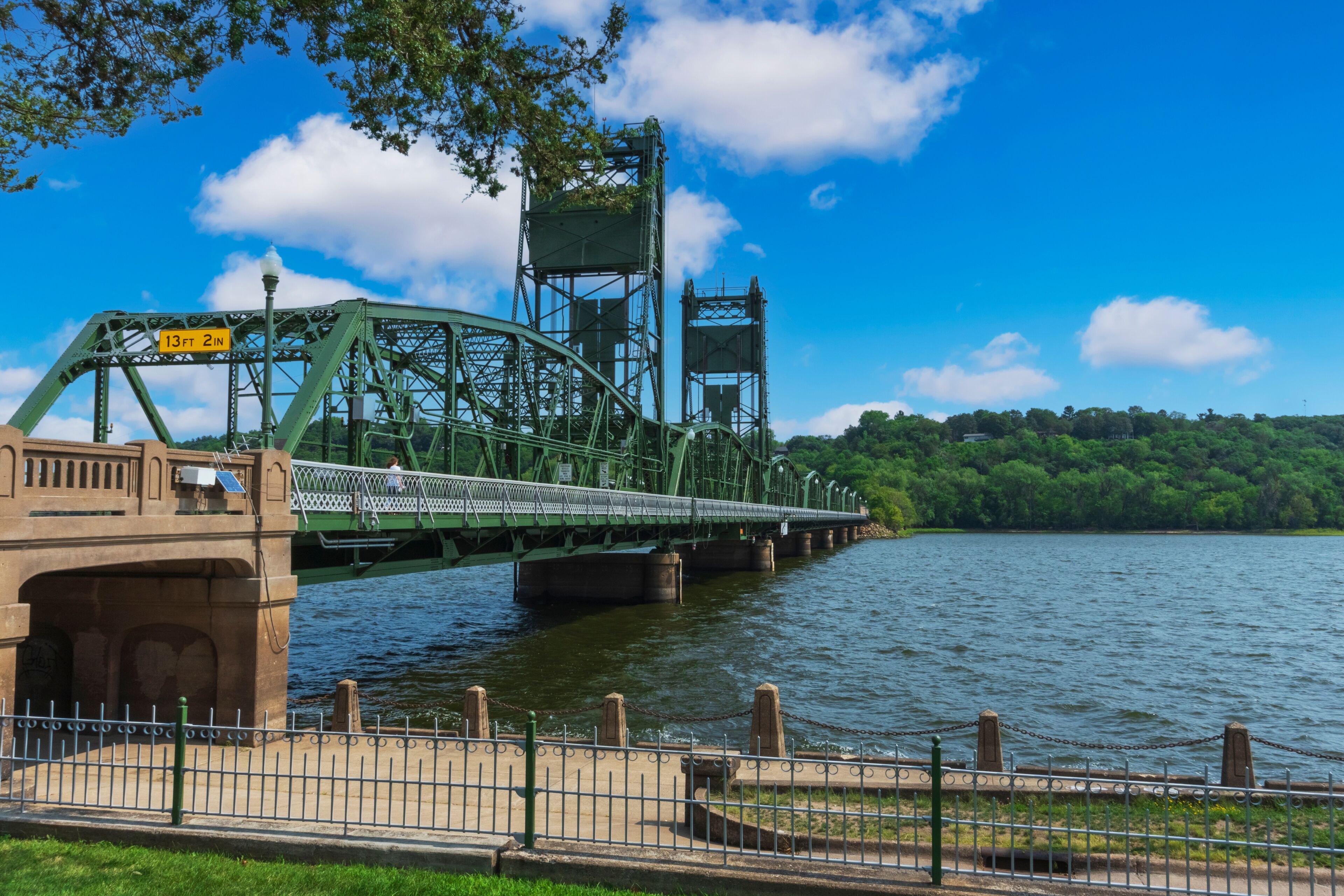 A green metal bridge over a river with a clear sky.
