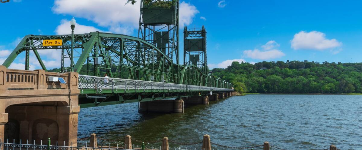 A green metal bridge over a river with a clear sky.