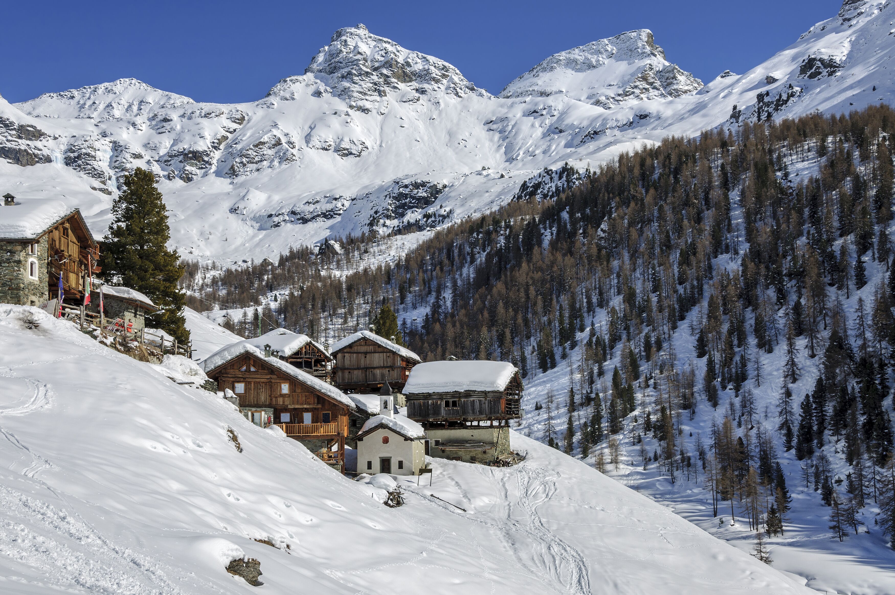 A snow-covered mountain village with wooden houses and a clear blue sky.