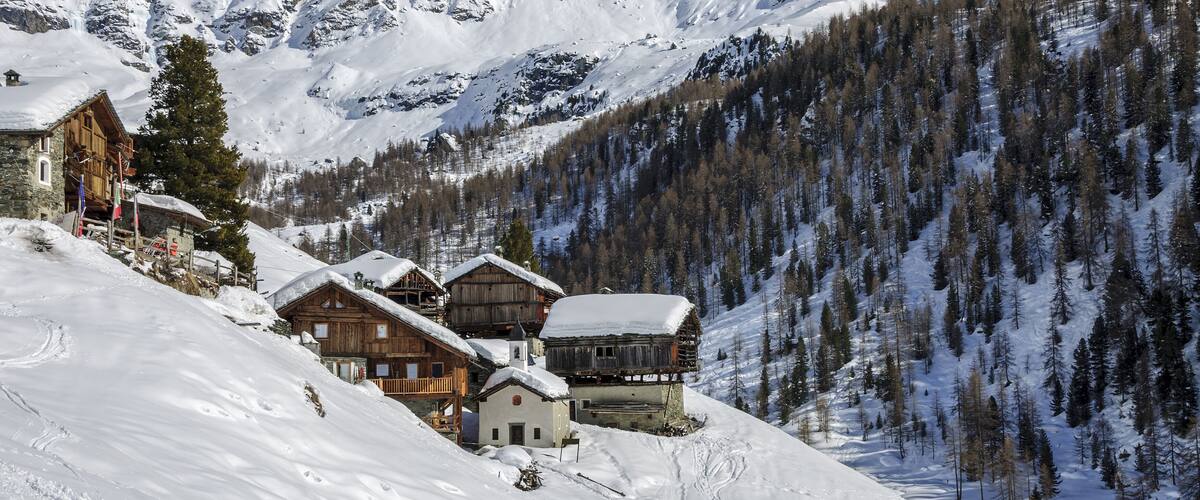 A snow-covered mountain village with wooden houses and a clear blue sky.