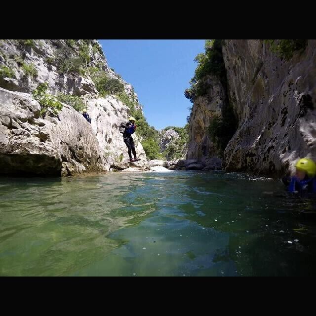 A canyon with clear water, rocky cliffs, and a person climbing.