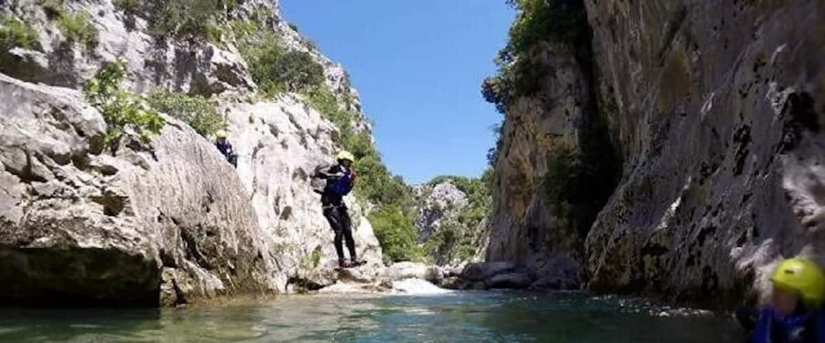 A canyon with clear water, rocky cliffs, and a person climbing.