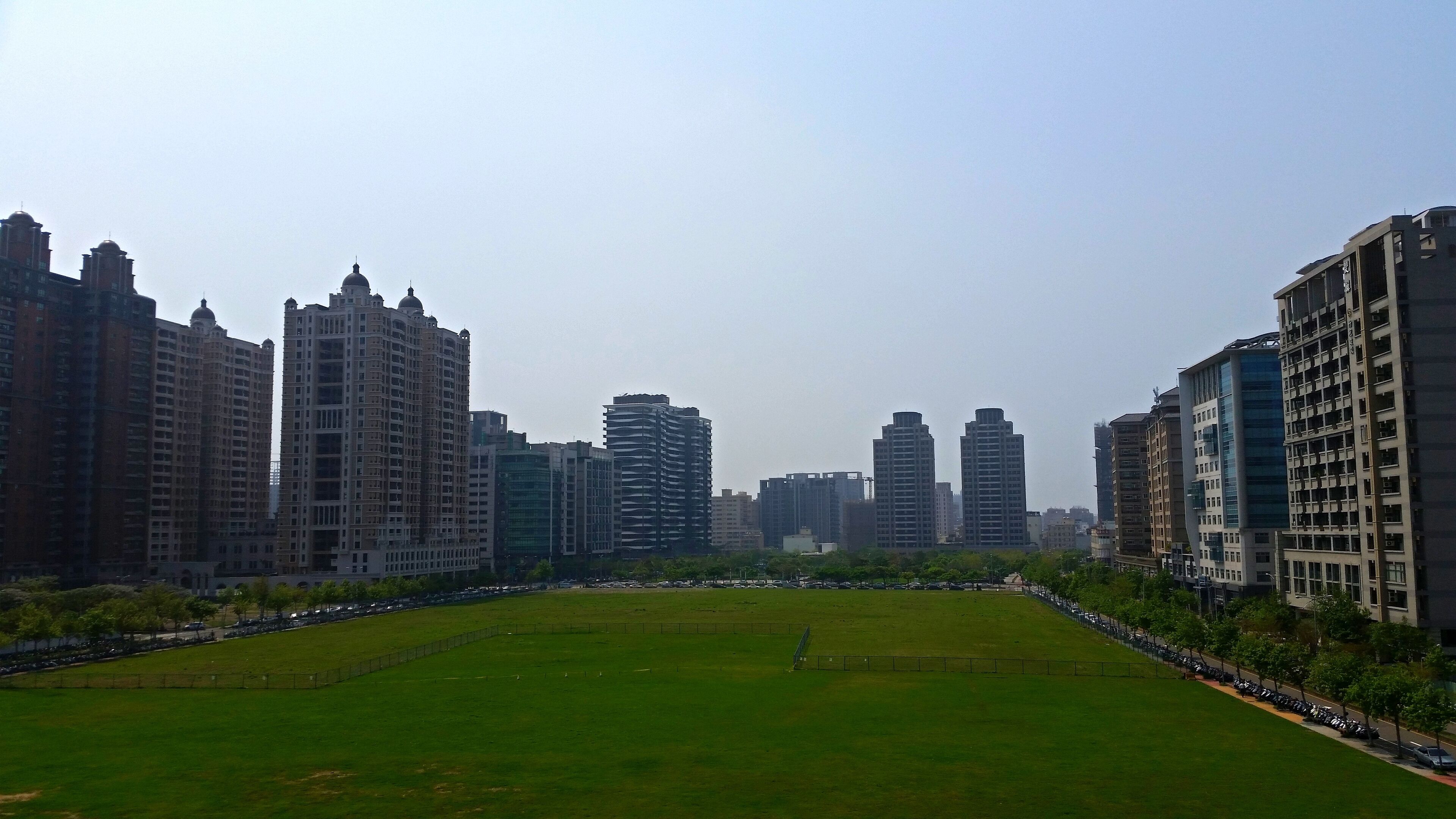 A cityscape with a large green park in the foreground and tall buildings in the background.