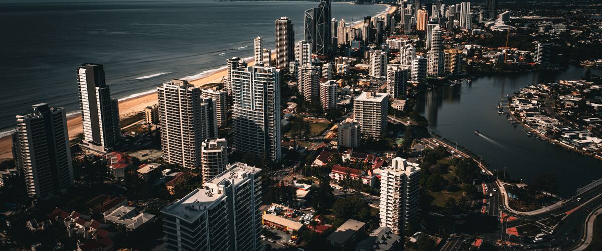 A coastal cityscape with high-rise buildings, a beach, and a river.