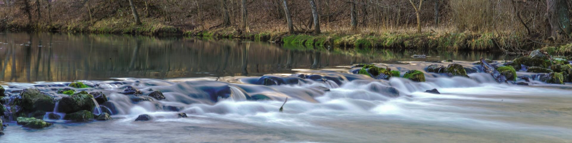 A river with a smooth flow over rocks, surrounded by a forested area.