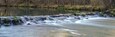 A river with a smooth flow over rocks, surrounded by a forested area.