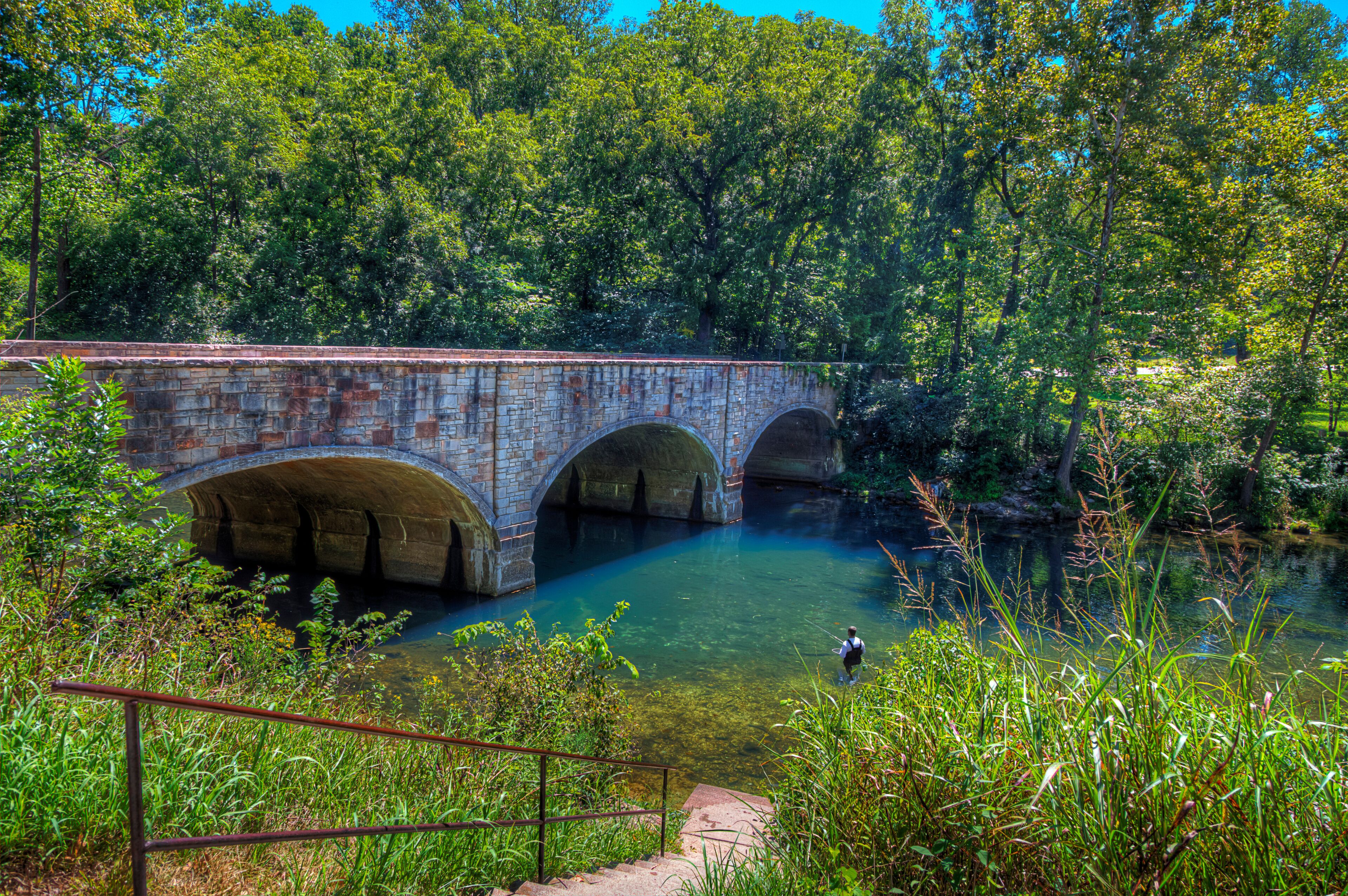 A stone bridge over a clear river surrounded by lush greenery.