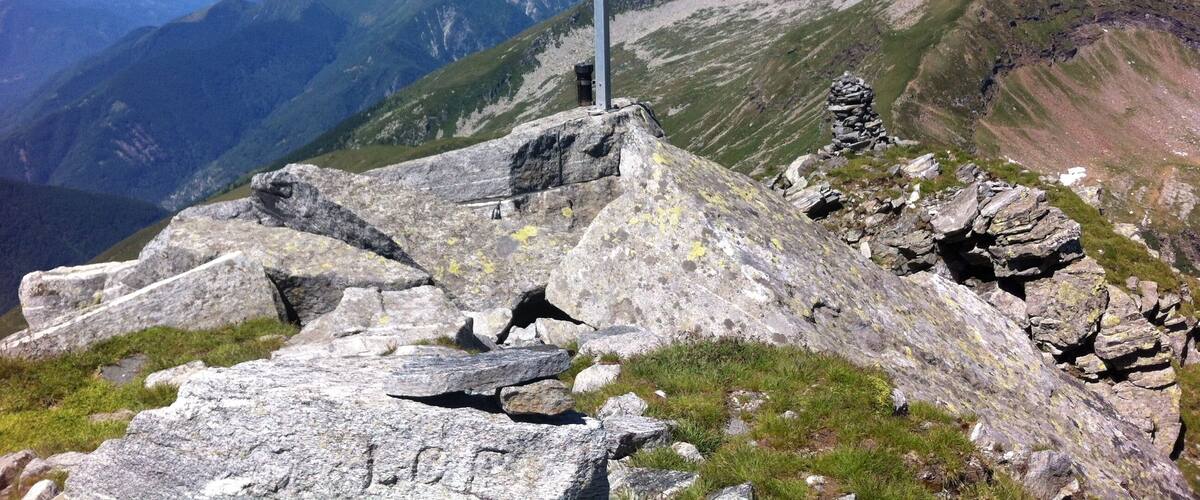 A cross on a mountain peak with a view of snow-capped mountains in the background.