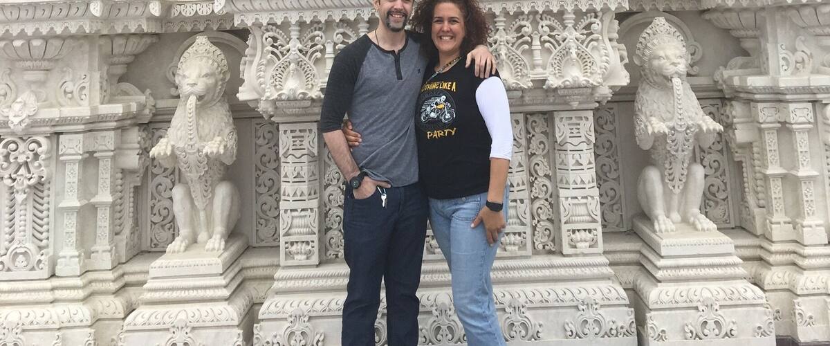 A couple standing in front of a detailed white temple facade with intricate carvings and statues.