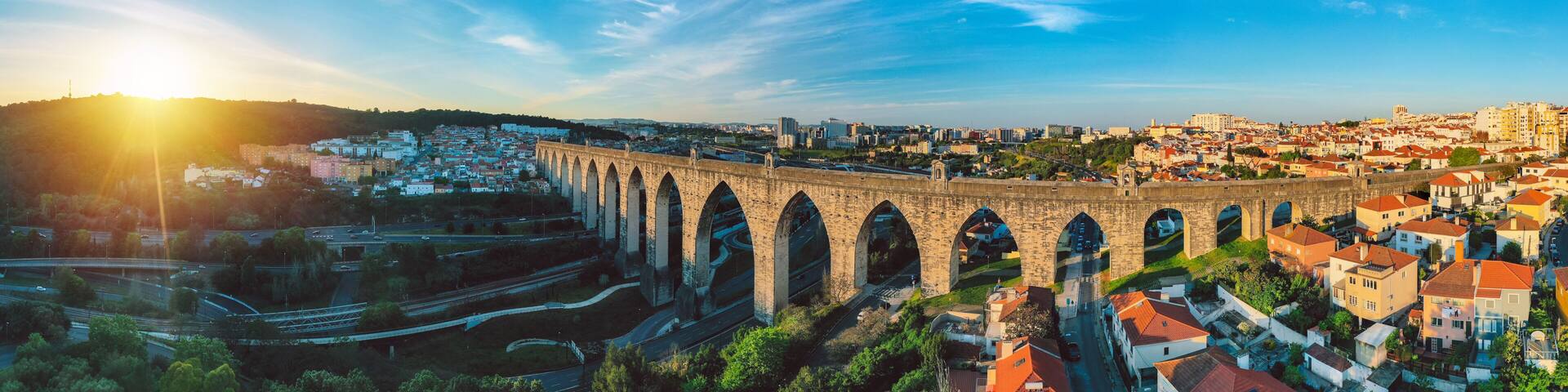 A bridge with multiple arches spanning a valley, surrounded by a cityscape with buildings and roads.