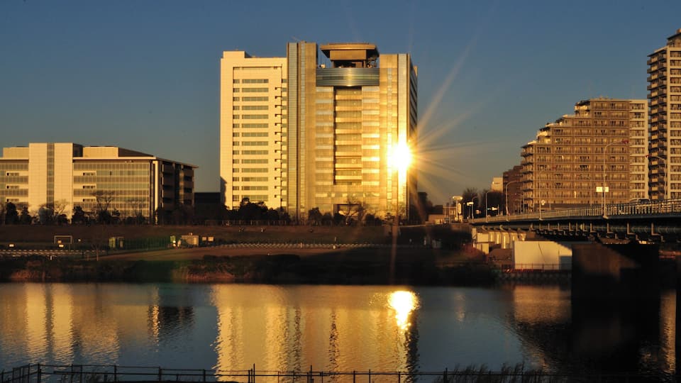 A cityscape with modern buildings and a river reflecting the sunset.