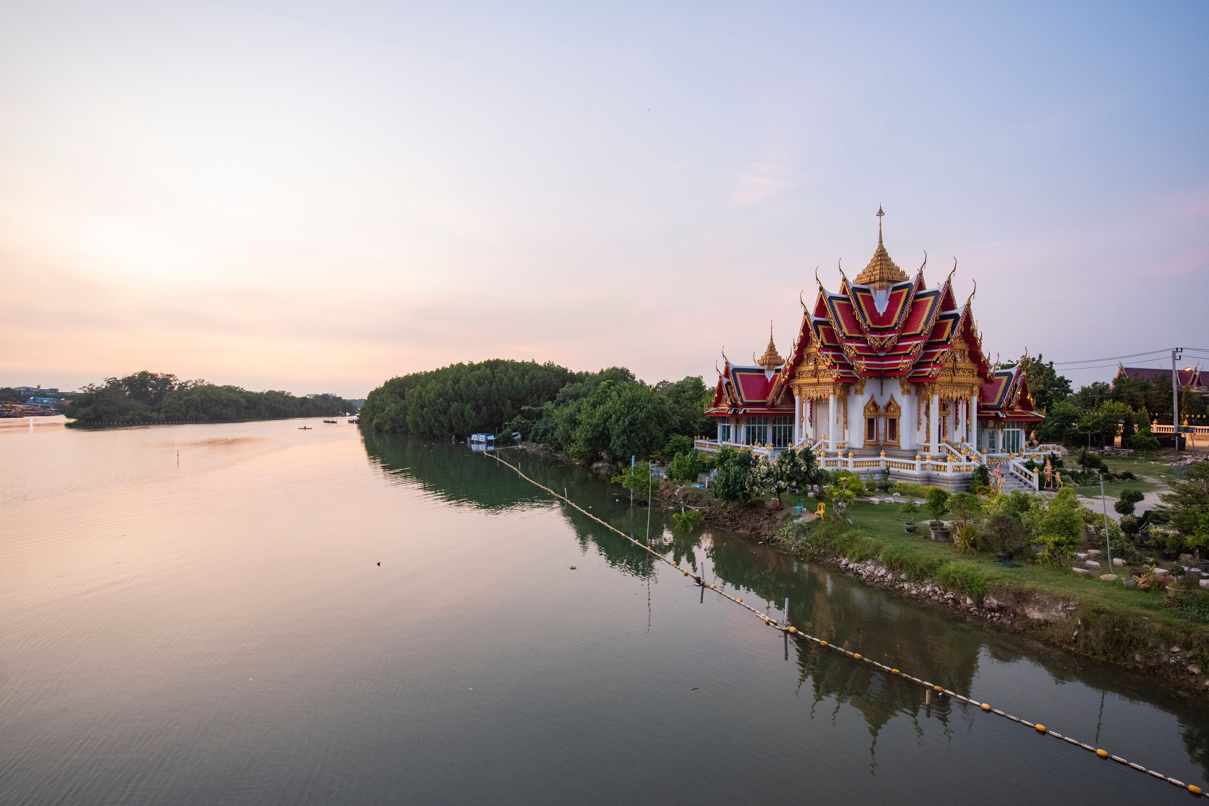 A temple with a golden roof and red and white walls by a calm river.