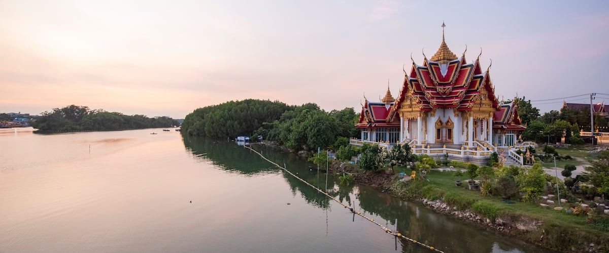 A temple with a golden roof and red and white walls by a calm river.