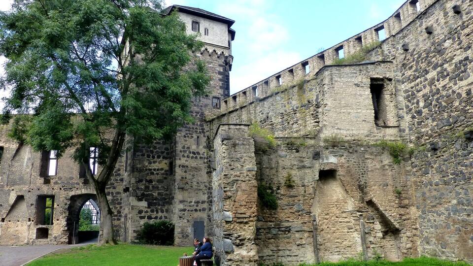 A historic stone wall with a tree in the foreground and a building in the background.