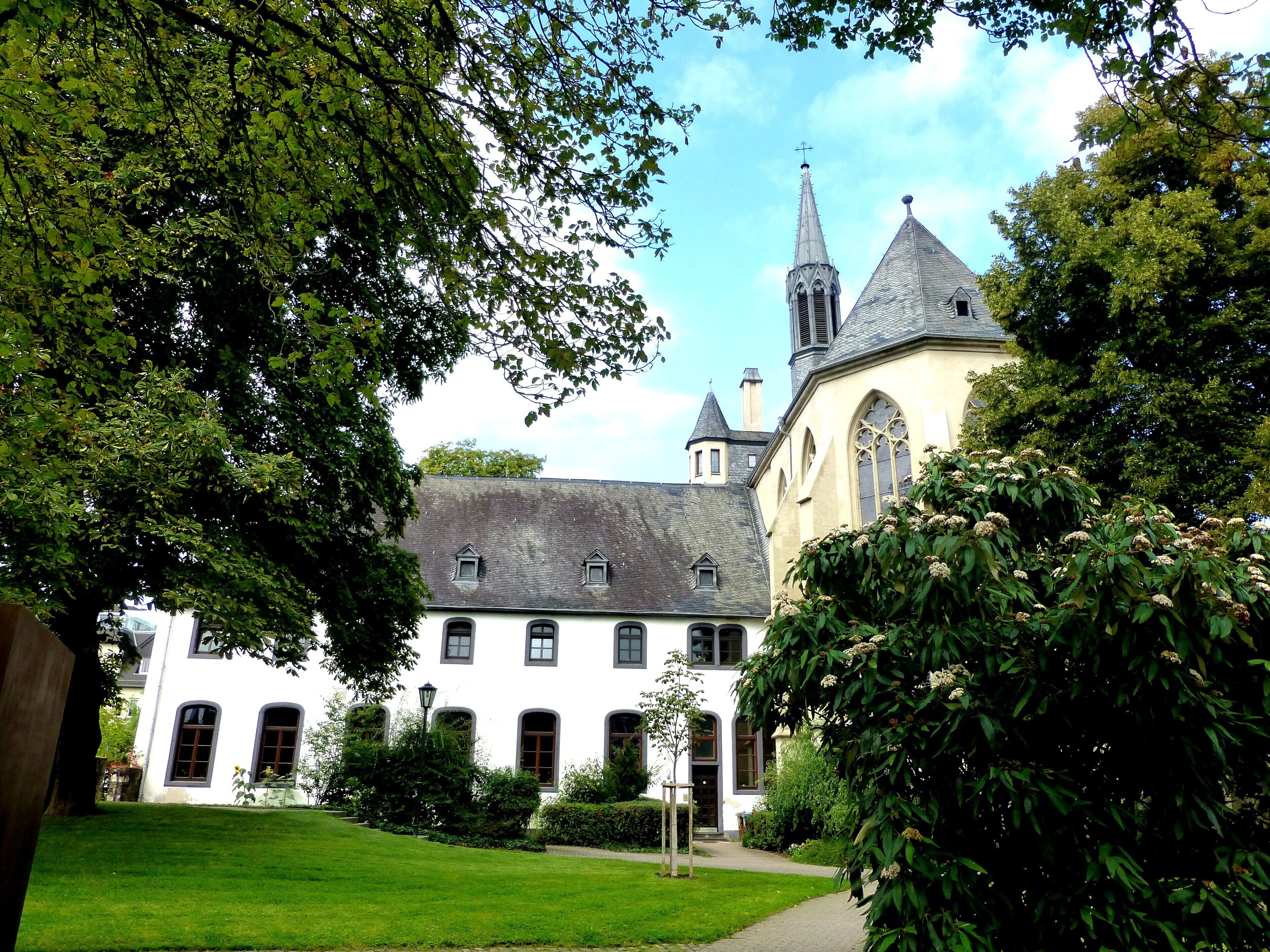 A historic building with a tower and a white facade, surrounded by lush greenery.