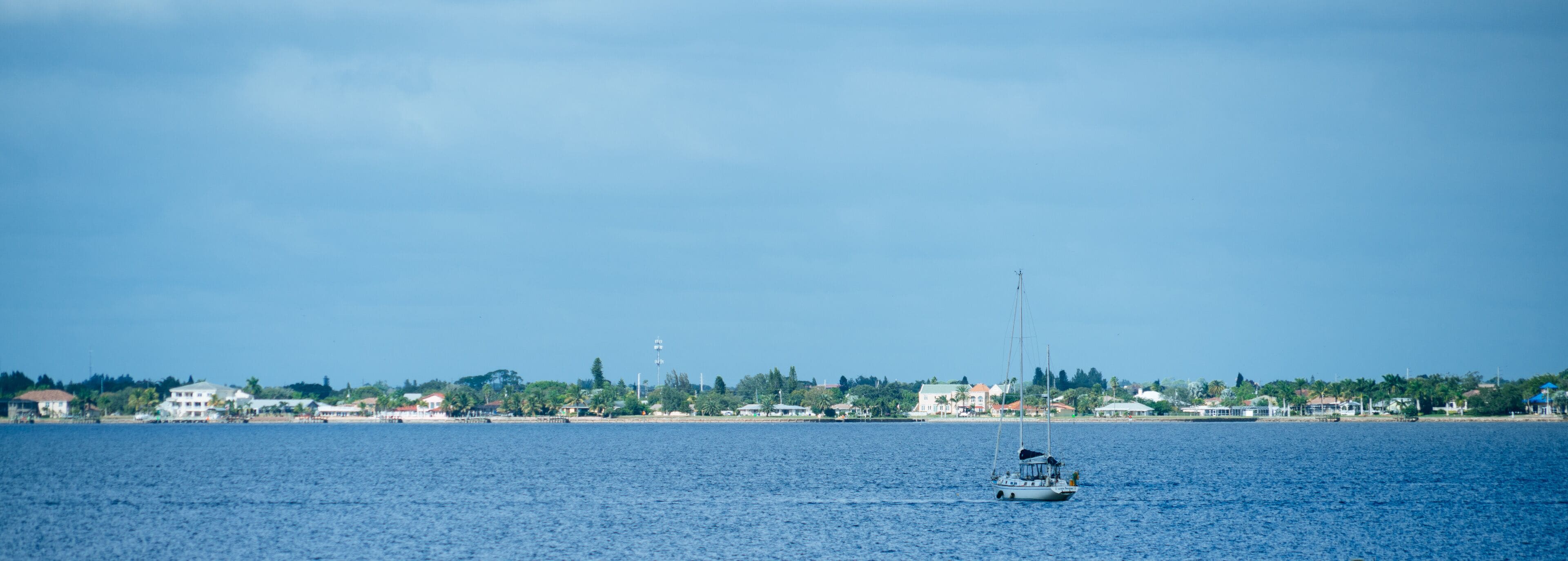 A sailboat on a calm sea with a coastal town in the background.