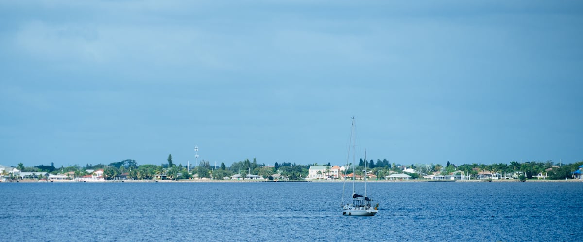 A sailboat on a calm sea with a coastal town in the background.