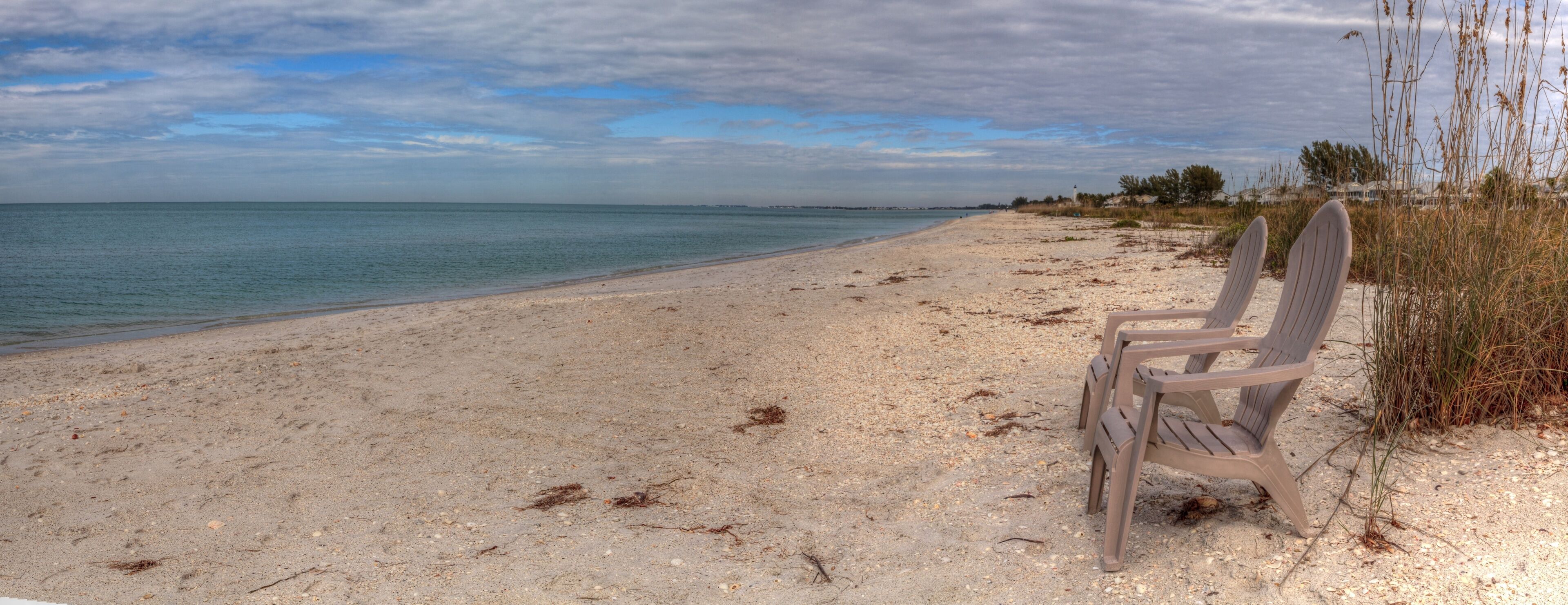 A beach with a single plastic chair, clear blue water, and a cloudy sky.
