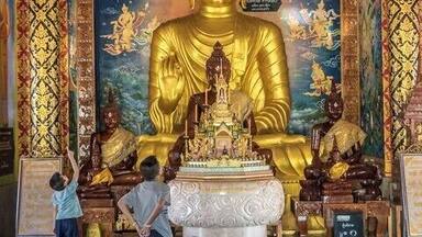 Una gran estatua dorada de Buda en un templo con pinturas murales intrincadas y decoraciones ornamentales.