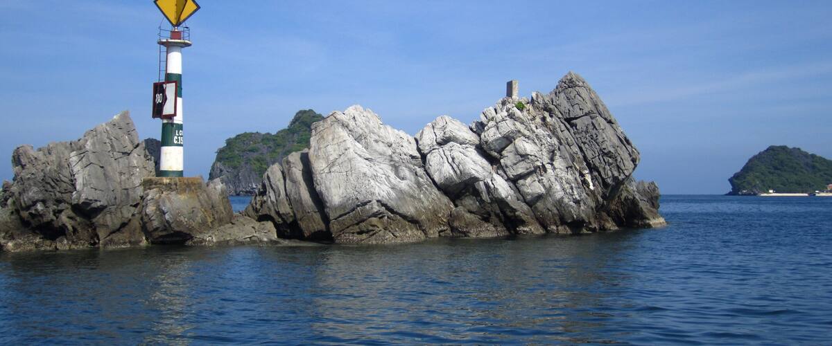 A lighthouse on a rocky outcrop with clear blue water and a distant island.