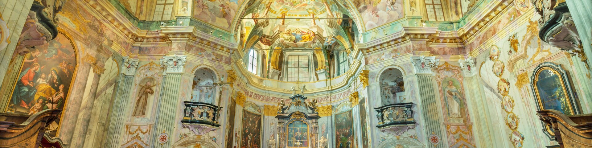 Interior de iglesia ornamentado con frescos detallados, un altar central y filas de bancas.