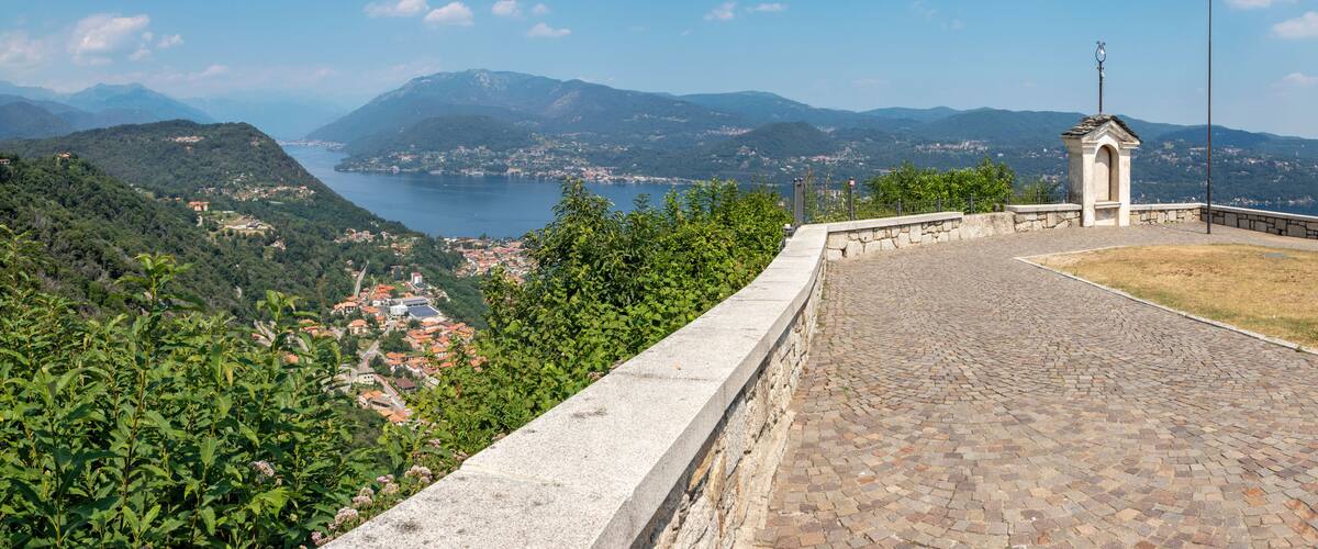 A scenic overlook with a view of a lake, mountains, and a small chapel.