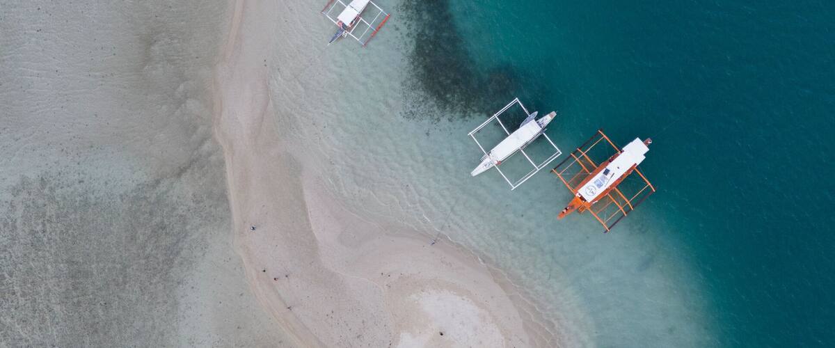 An aerial view of a beach with several boats anchored near the shore.