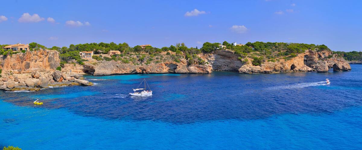 A coastal landscape with rocky cliffs, clear blue waters, and houses on the hillside.