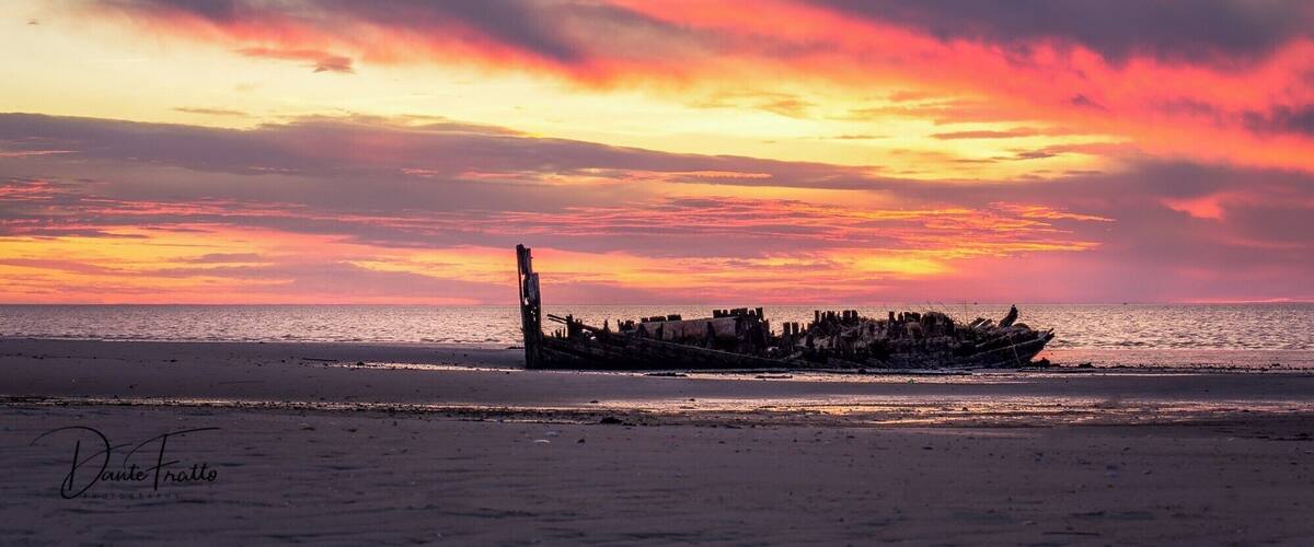 A sunset over a beach with a shipwreck.