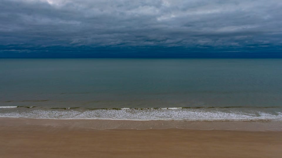 A beach with a calm sea under a cloudy sky.