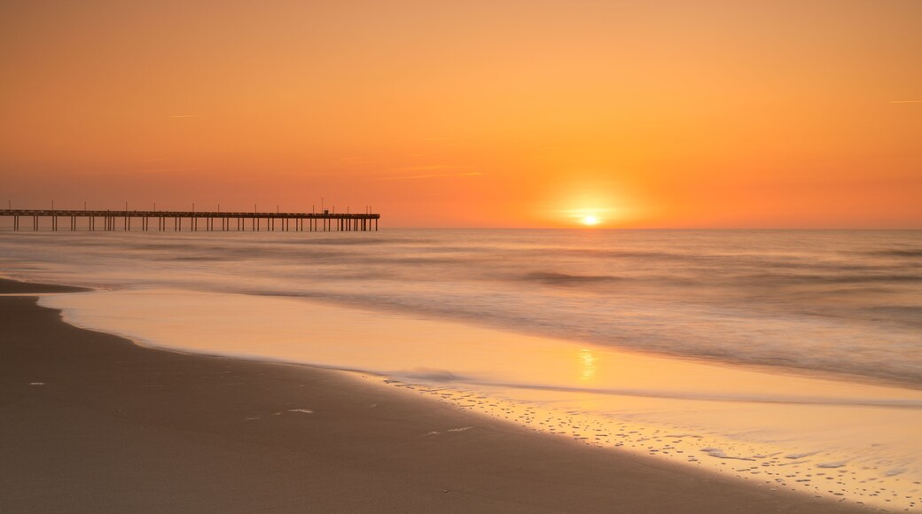A sunset over a beach with waves and a pier.