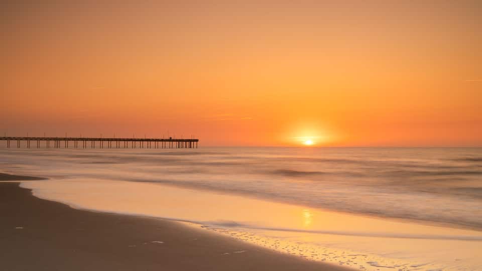 A sunset over a beach with waves and a pier.