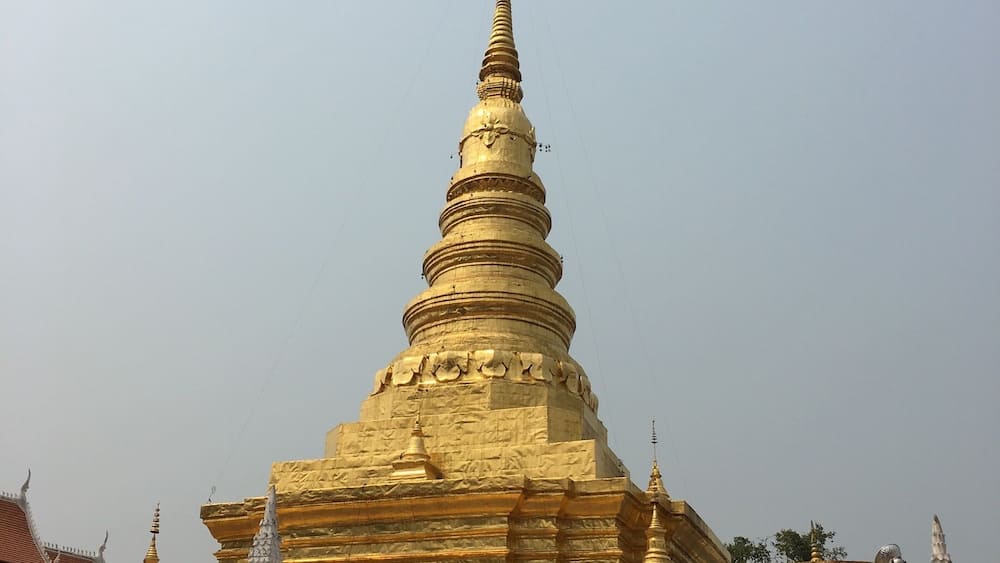 A large golden stupa with a pointed spire, surrounded by white walls and smaller structures.