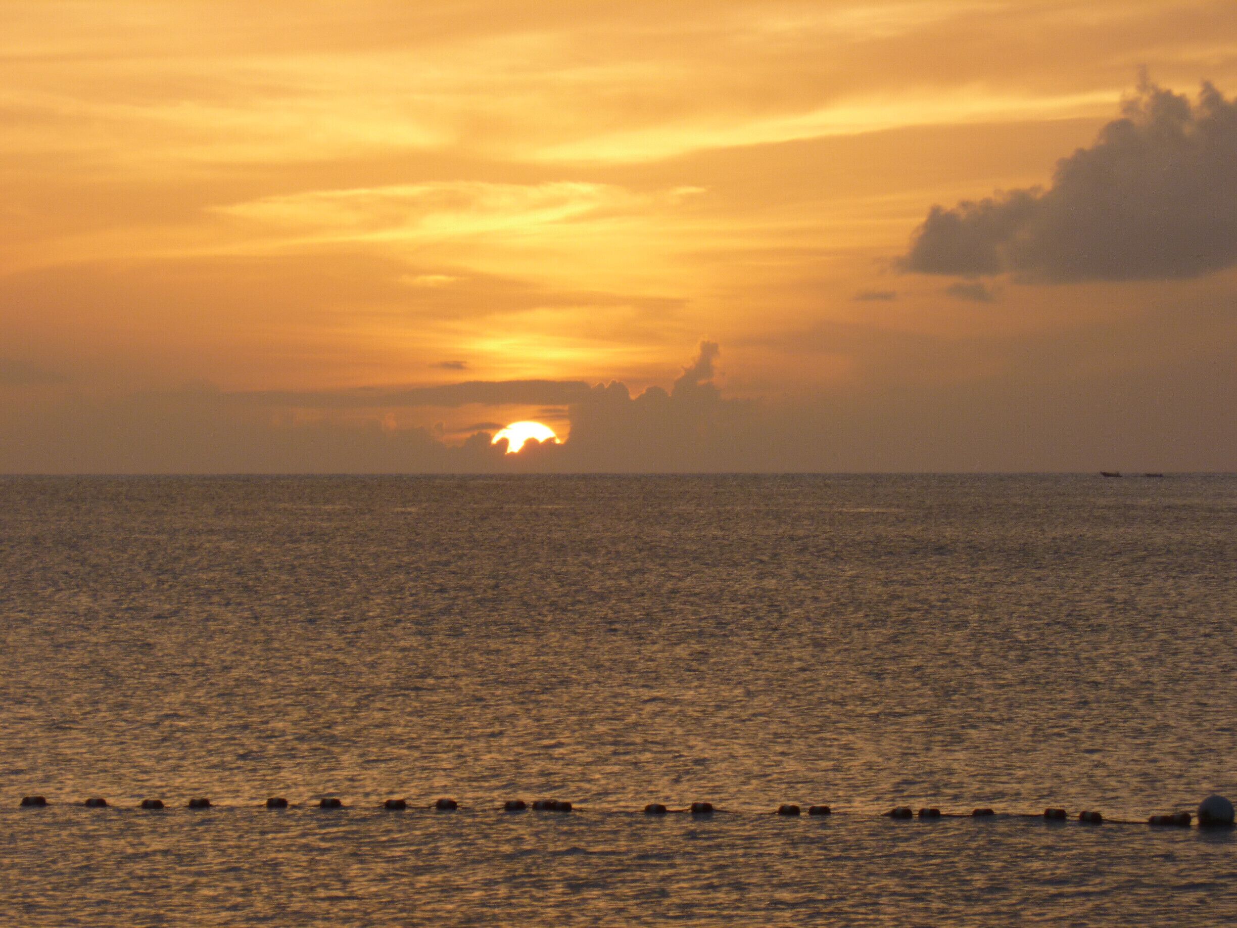 A sunset over a calm sea with a row of buoys in the foreground.