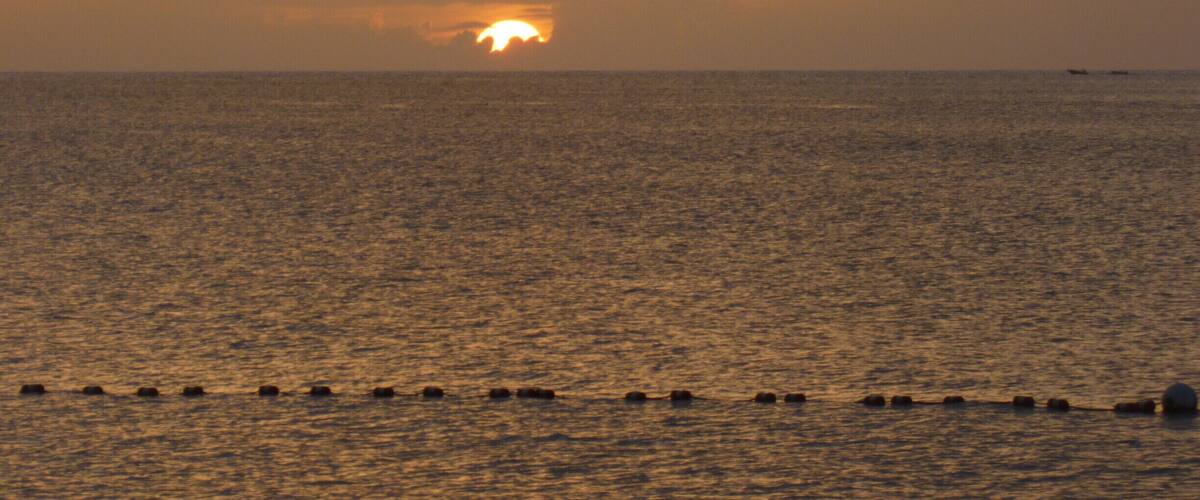 A sunset over a calm sea with a row of buoys in the foreground.