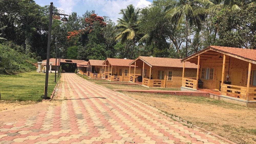 Une rangée de cabanes en bois aux toits rouges, un chemin pavé et une végétation luxuriante en arrière-plan.