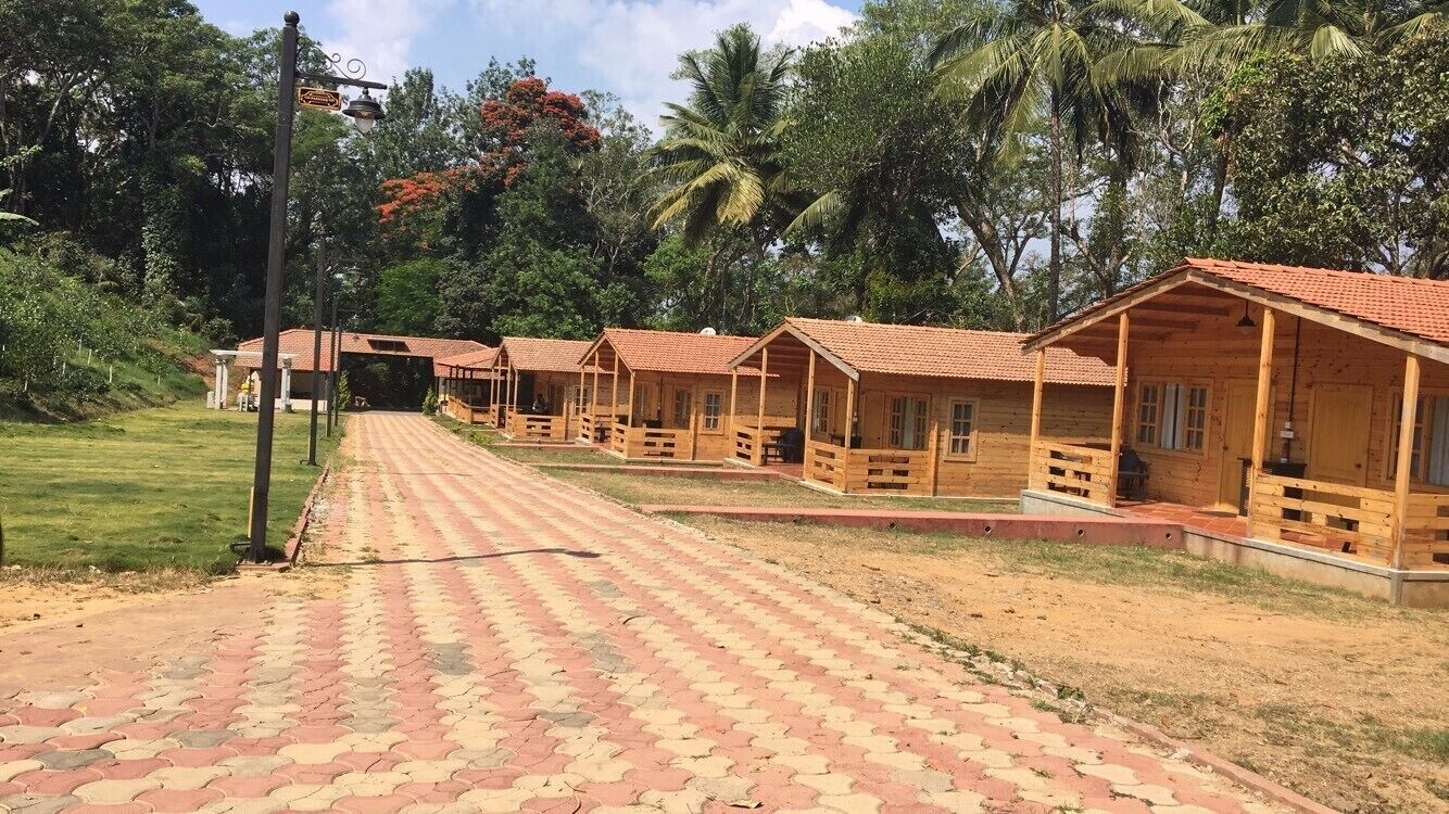 A row of wooden cabins with red roofs, a paved pathway, and lush greenery in the background.