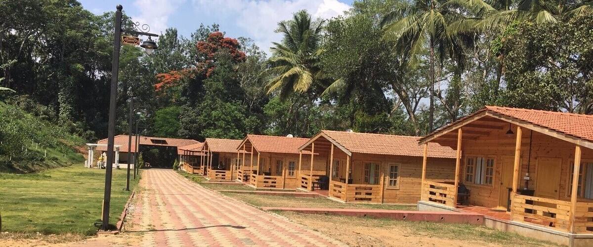 A row of wooden cabins with red roofs, a paved pathway, and lush greenery in the background.