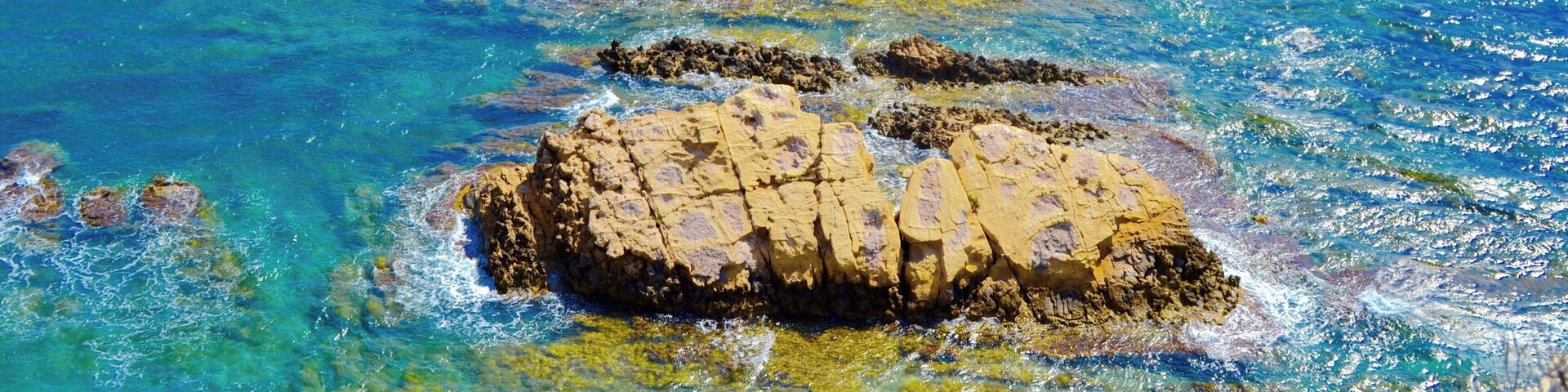 A rocky coastline with clear blue waters and a prominent rock formation.