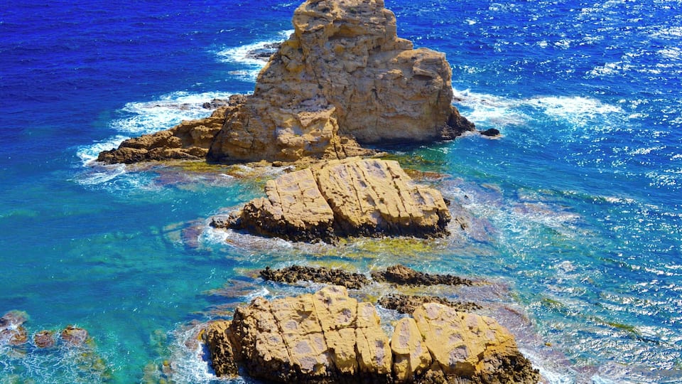 A rocky coastline with clear blue waters and a prominent rock formation.