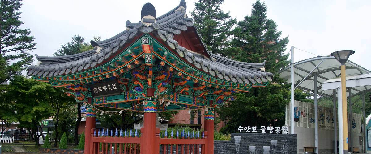 A traditional Korean pavilion with ornate roof and colorful decorations, surrounded by a paved walkway and greenery.
