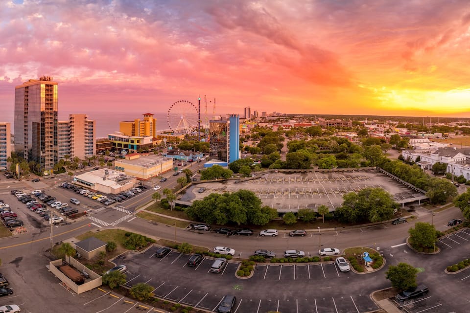 A coastal cityscape with a roller coaster, parking lots, and a sunset sky.