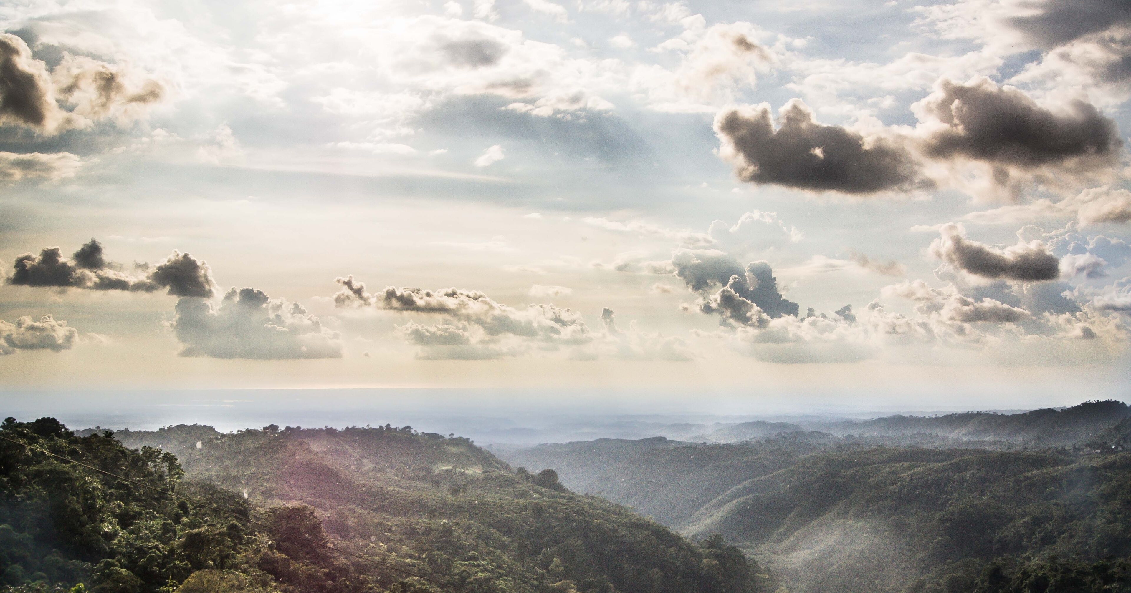 A mountainous landscape with dense forests and a cloudy sky.