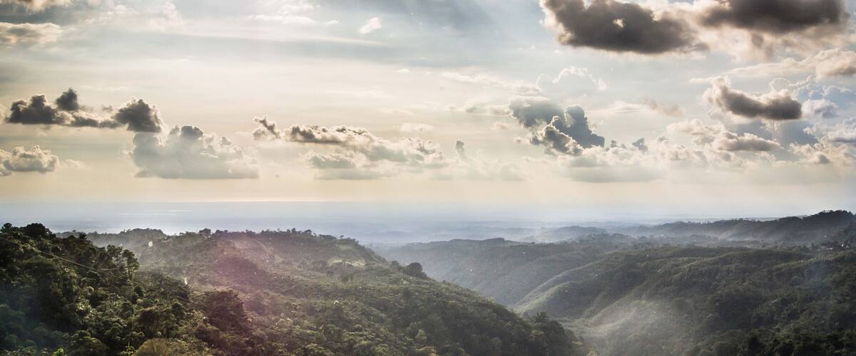 A mountainous landscape with dense forests and a cloudy sky.