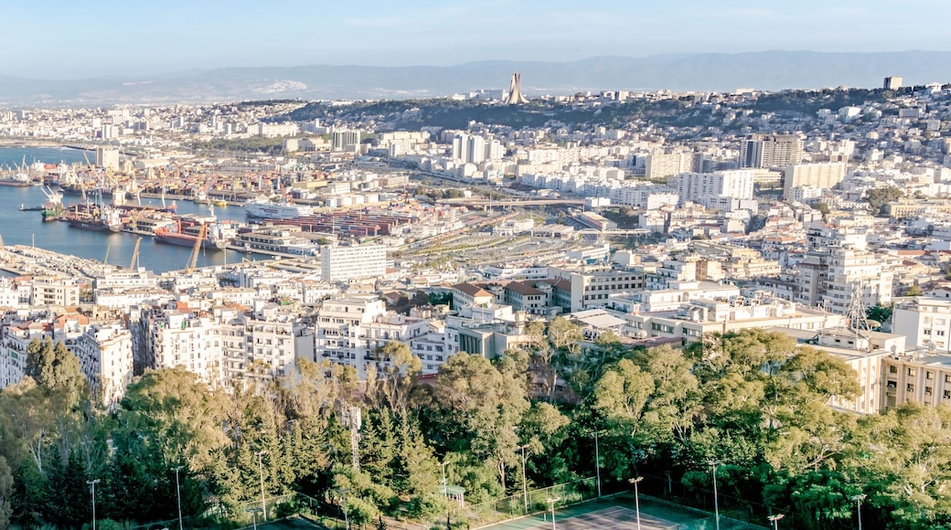Algiers sea bay and pier port, aerial view on the capital city buildings, trees and Mediterranean blue water ships and boats. The Great mosque and the Martyr's Memorial monument.